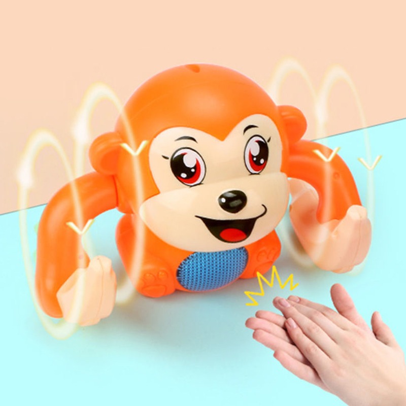 Un jouet en forme de singe orange avce des bananes dans les mains, sur fond bleu, des mains qui claquent des mains.