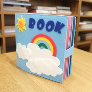 Livre tissu montessori, avec des activités éducatives, avec un nuage et un arc en ciel sur la page de couverture, il s'agit d'un livre bleu avec marqué dessus "book"