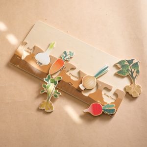 Jouet puzzle en bois rectangulaire avec différents légumes à placer dans leur espace dédié. Posé sur un sol beige.